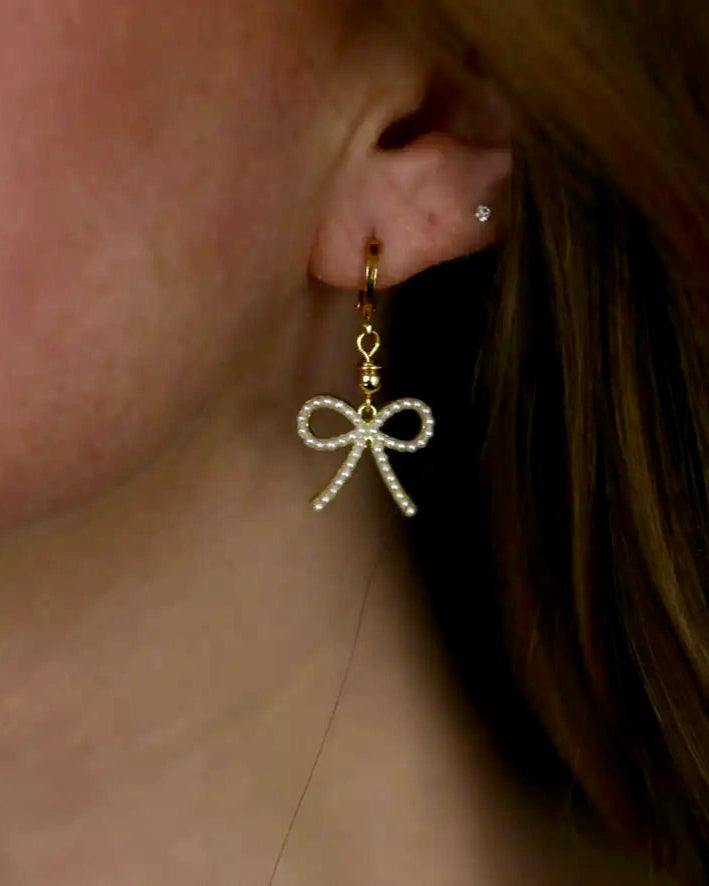 Gold bow-shaped earring worn by a person