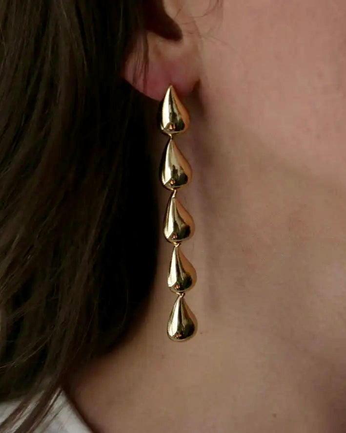 Gold earrings worn by a person with a neutral background
