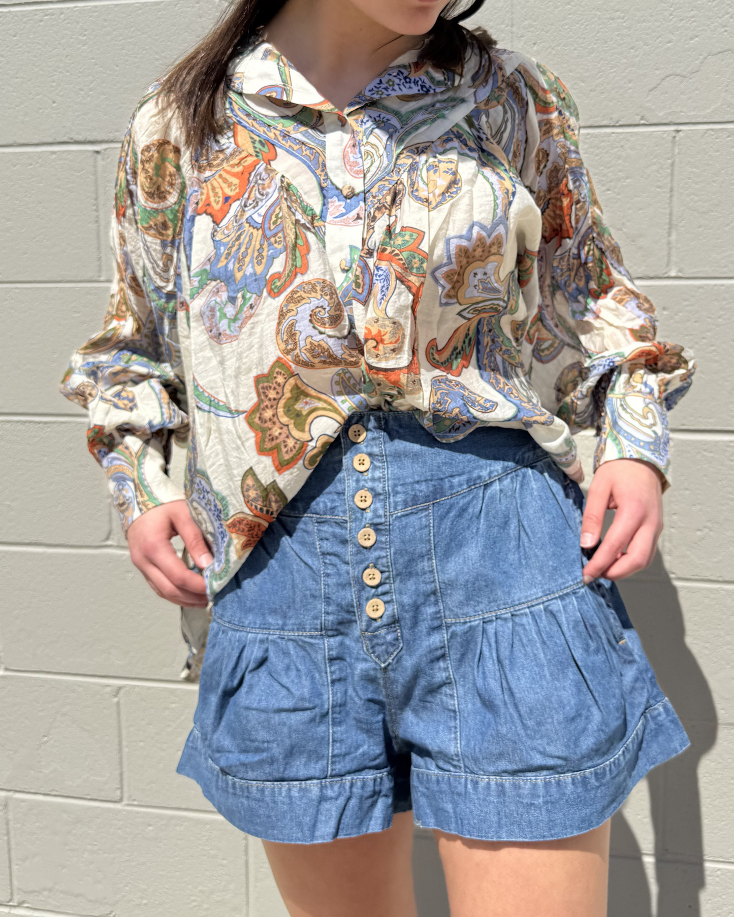 A pair of blue denim shorts with pleated details and buttons, paired with a floral patterned shirt.