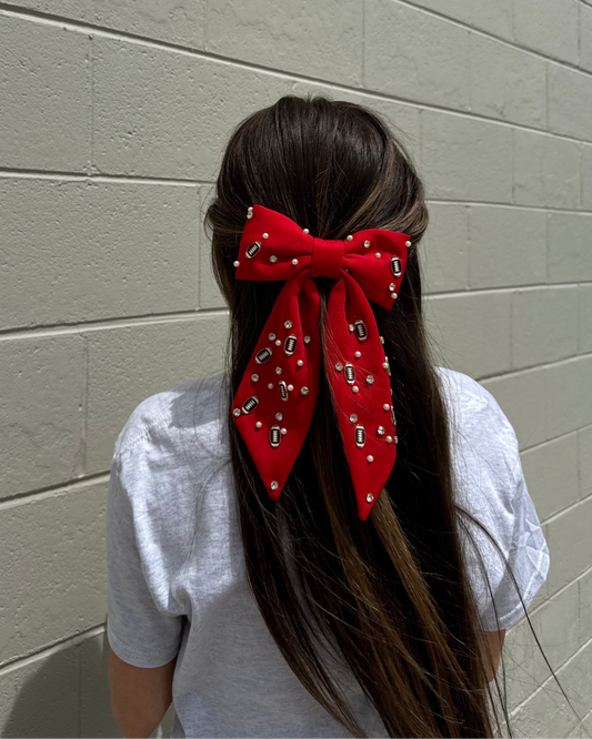 Person with a red hair bow featuring silver studs against a light gray wall
