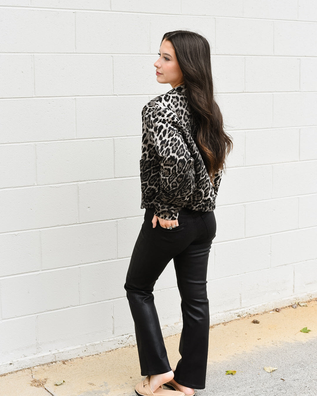 Woman wearing a leopard print jacket and black pants against a white wall.