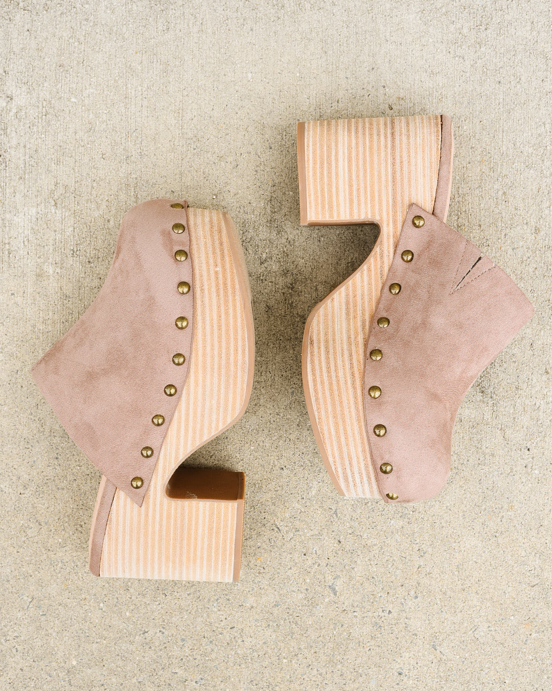 Pair of beige suede high-heeled shoes with wooden soles on a beige surface