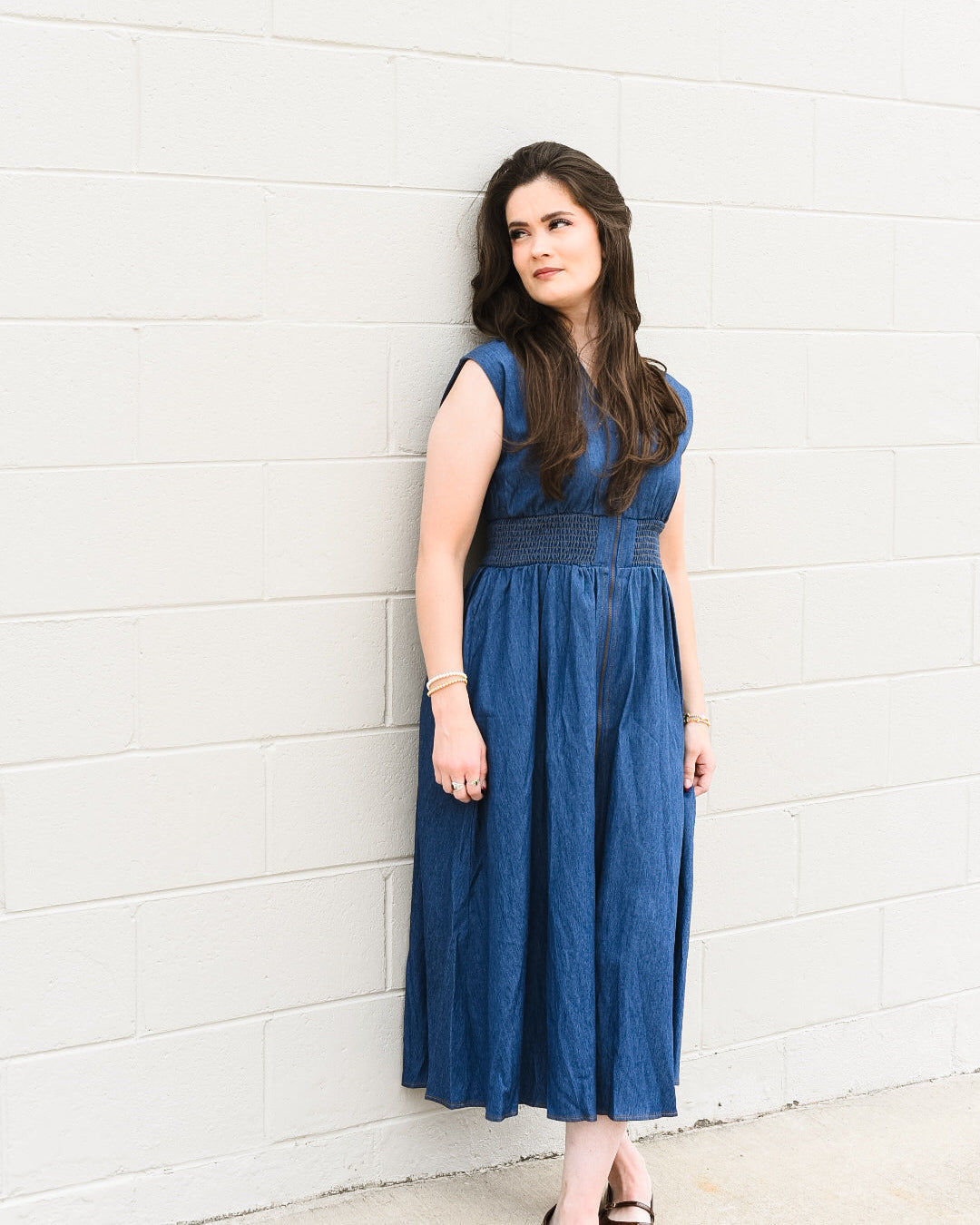 Woman in a blue dress standing against a white wall