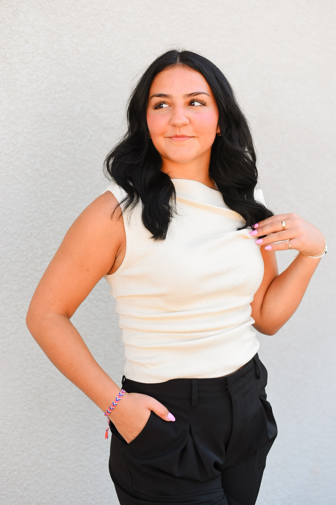 Woman wearing a white sleeveless top and black pants against a plain background