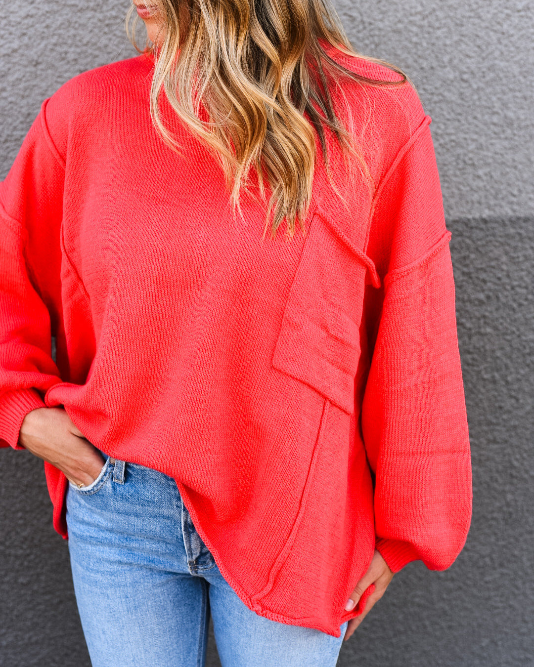 Person wearing a red sweater and blue jeans against a gray wall