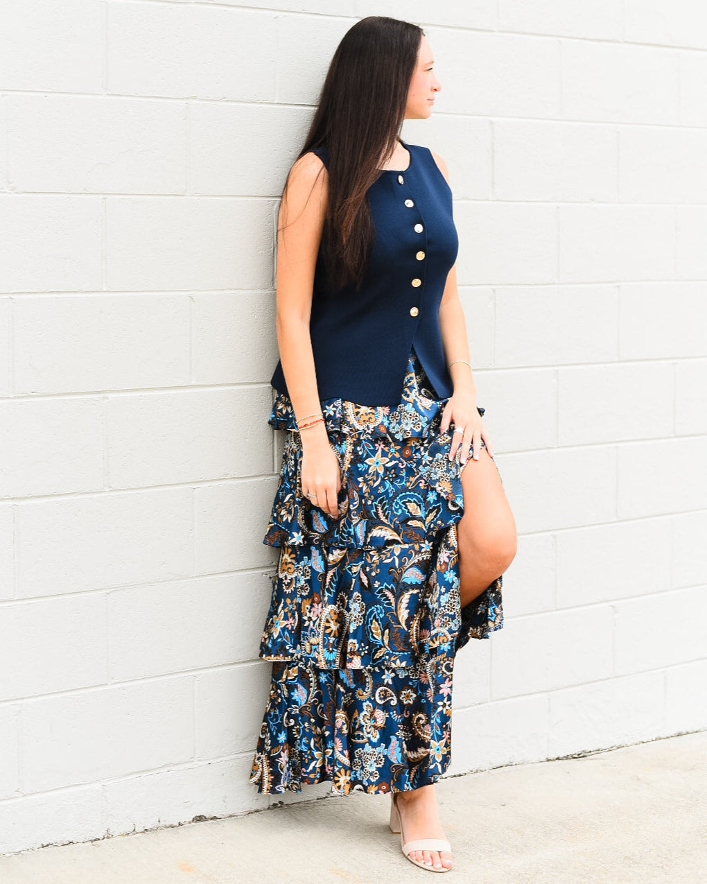 Woman wearing a navy top and floral skirt against a white wall