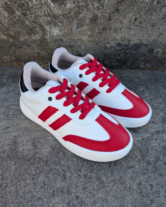 A pair of white sneakers with red stripes and laces, placed on a concrete surface.