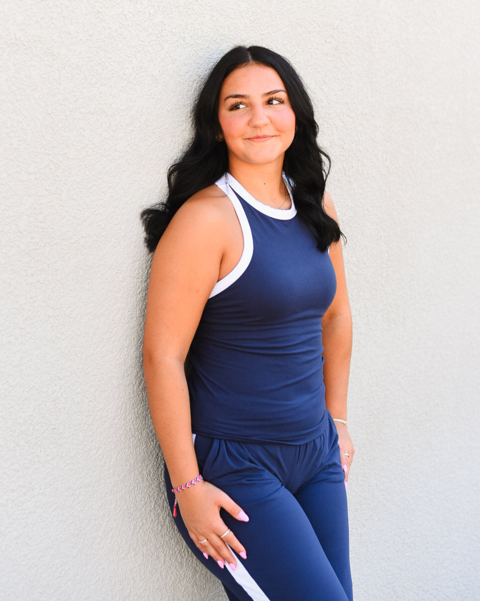 Woman wearing a blue athletic outfit with white accents against a light gray wall.