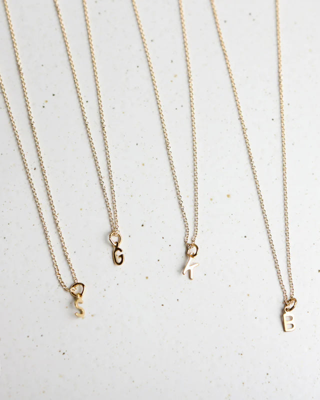 Four gold necklaces with initial pendants on a light gray background
