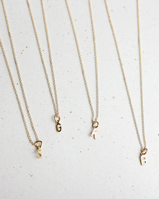 Four gold necklaces with initial pendants on a light gray background