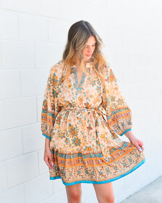 Woman wearing a patterned dress standing against a white tiled wall.