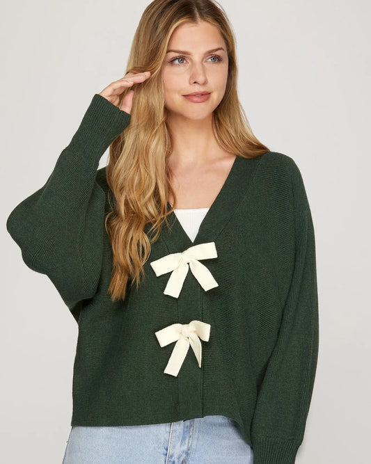 Woman wearing a green sweater with white bows on a plain background