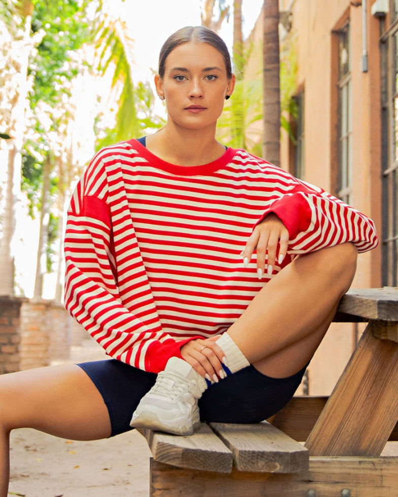Person wearing a red and white striped sweater sitting on a wooden bench outdoors.